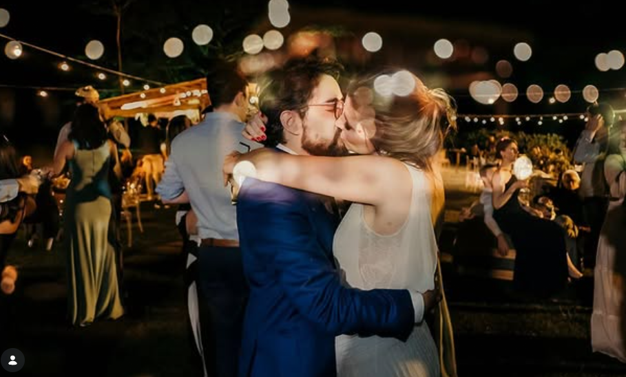 Bride and groom kissing under string lights